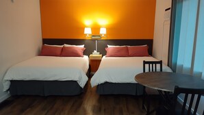 Habitación de hotel con dos camas, una mesita y una silla. Dos lámparas de pared sobre las camas.