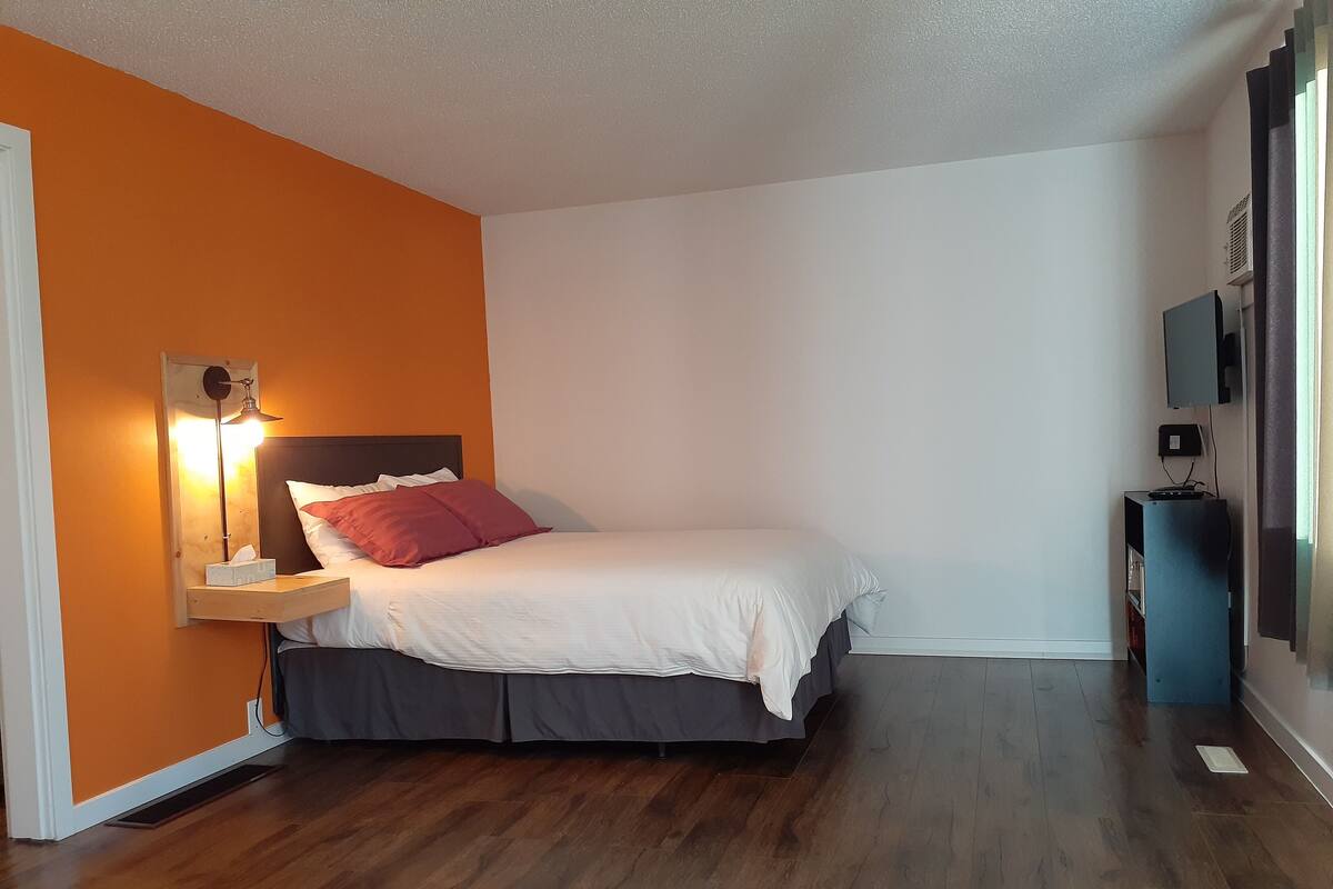 A bedroom with a bed, a bedside table with a lamp, and a wall-mounted TV.