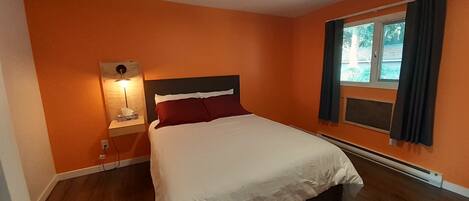 A bedroom with a bed, a nightstand, a lamp, and a window with curtains.