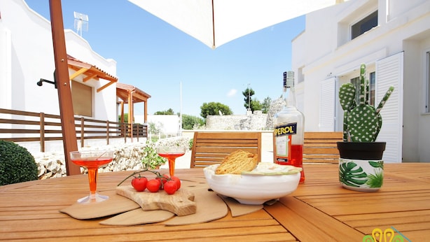 A wooden table with a bottle of Perol, a cactus, a bowl of food, and a glass of red drink. - Pavon House Blue -Villetta 80 meters from the sea, 3 km from Torre San Giovanni beaches (Alliste)