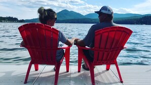 Twee personen zitten in rode stoelen, gericht op een wateroppervlak met bergen op de achtergrond.