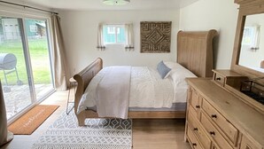 Een slaapkamer met een bed, een houten dressoir, een spiegel en een raam met gordijnen.