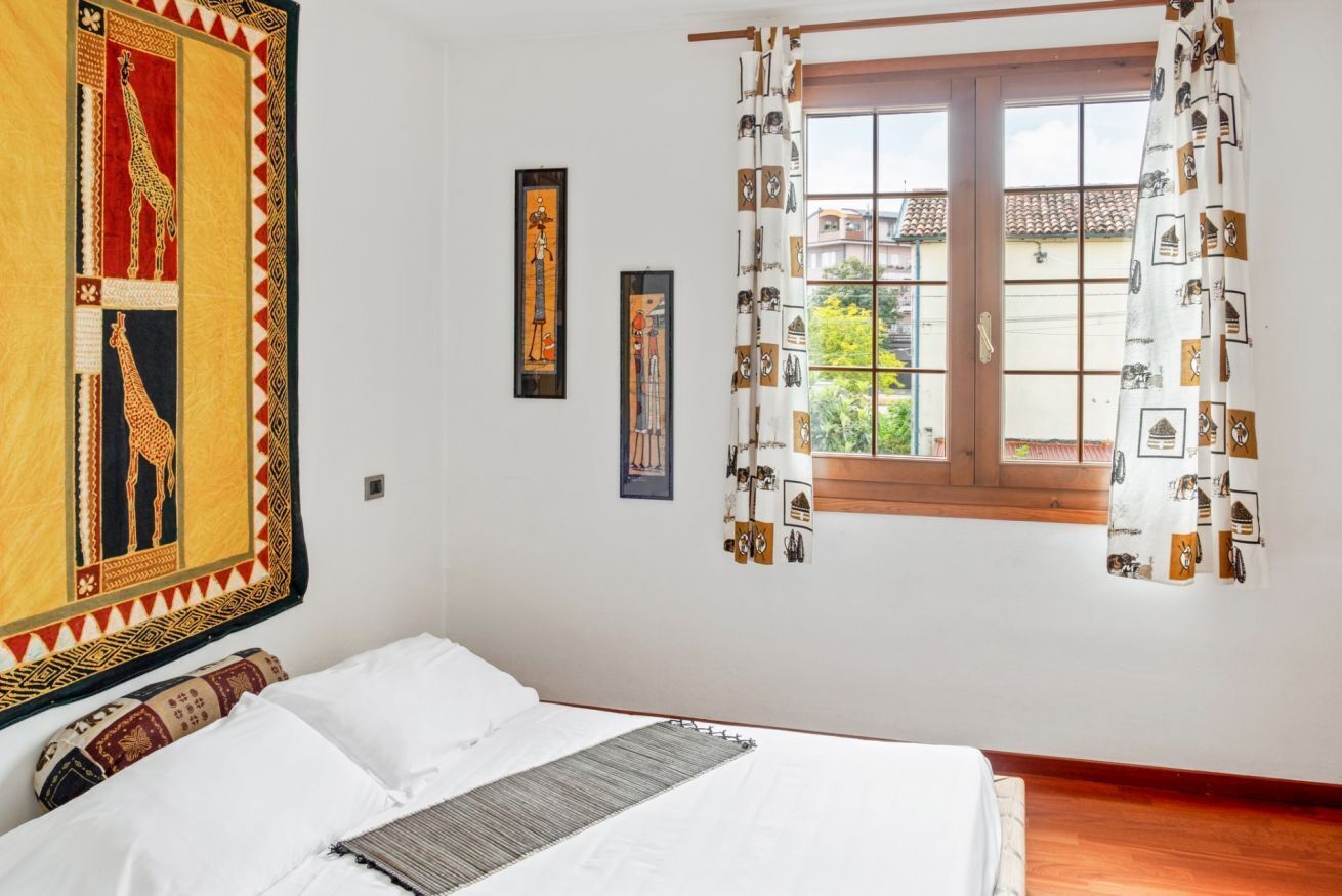 A bedroom with a bed, a window with curtains, and wall art.
