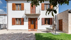 A two-story building with a balcony, a stone-paved entrance, and a small outdoor seating area. - GuestHost - Pretty and cozy private house is located in the central area in Abano Terme, a few steps from the Cathedral of San Lorenzo, Piazza Mercato and the Urban Thermal Park, in a quiet and relaxing neighbourhood, spacious and perfect for 6 people. T (Abano Terme)
