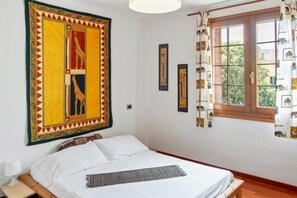 Un dormitorio con cama, mesita de noche, ventana con cortinas y adornos en la pared.