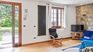 A room with a wooden floor, a stone wall, a TV stand, a blue sofa, a chair, and a window with curtains. - GuestHost - Pretty and cozy private house is located in the central area in Abano Terme, a few steps from the Cathedral of San Lorenzo, Piazza Mercato and the Urban Thermal Park, in a quiet and relaxing neighbourhood, spacious and perfect for 6 people. T (Abano Terme)