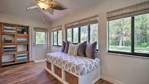 Quarto com um banco embutido, ventoinha no teto e grandes janelas com persianas.