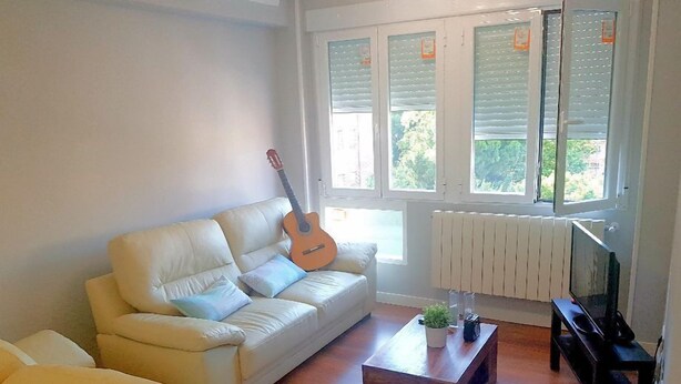 Una sala de estar con un sofá blanco, una mesa de centro con una planta y una guitarra apoyada contra el sofá.