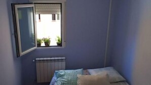 Un dormitorio con cama, ventana con vistas, radiador y lámpara de techo.