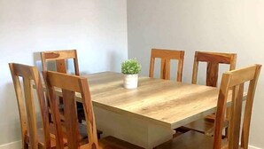 Una mesa rectangular de madera para comer con seis sillas, una planta pequeña en maceta y una pared blanca al fondo.