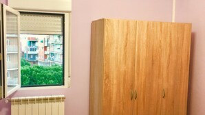 Un dormitorio con un armario de madera, una ventana con persianas, un radiador y una cama con edredón a cuadros.