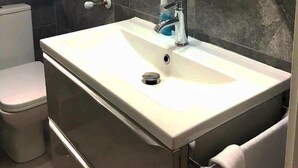 Un baño con un lavamanos blanco, un espejo, un perchero para toallas y un inodoro.