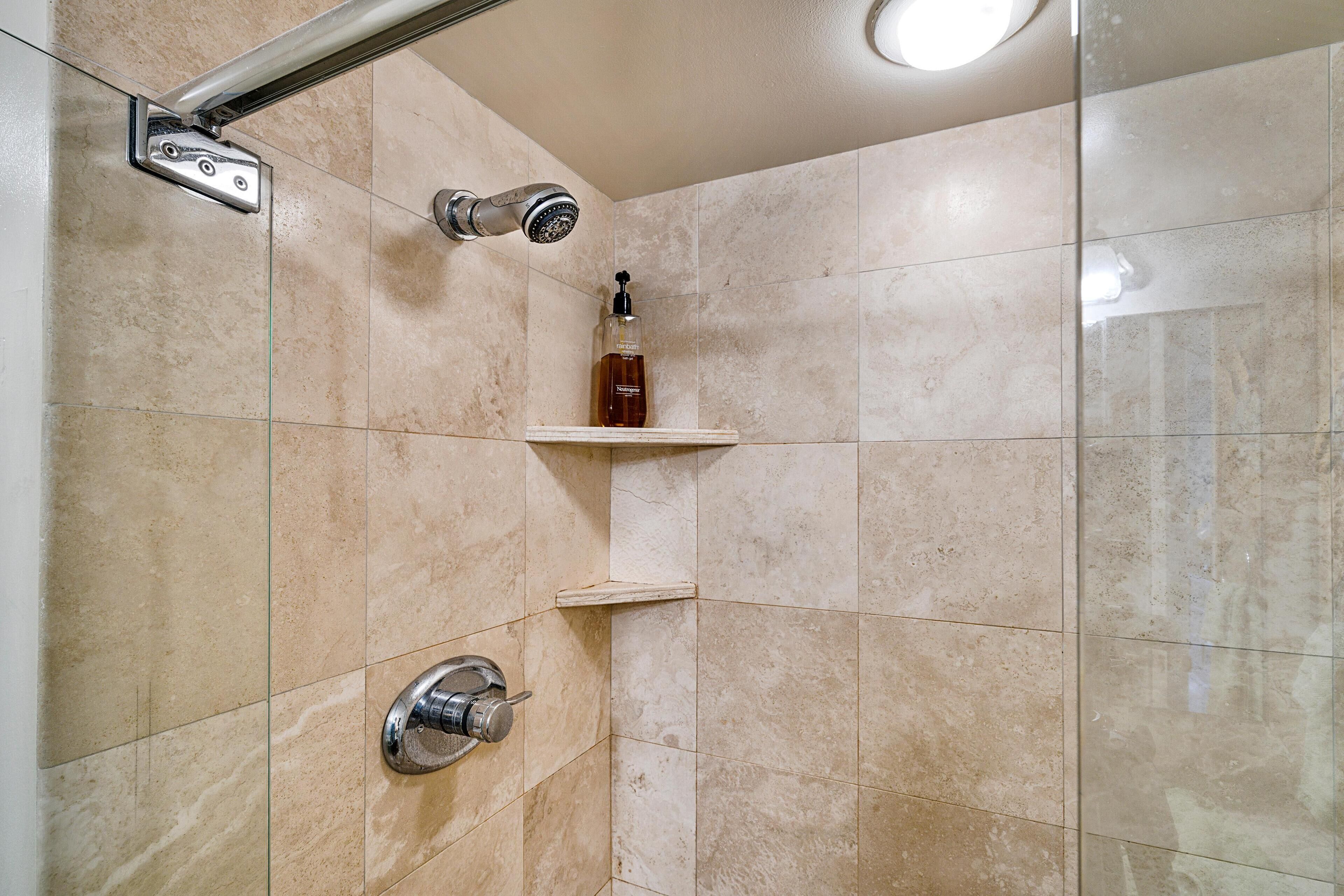 A shower area with a handheld showerhead, a wall-mounted faucet, and a soap dispenser on a shelf.