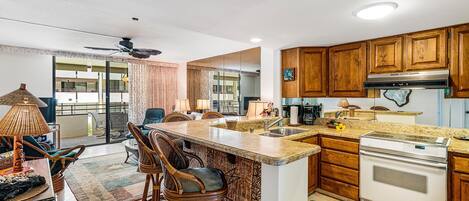 Una cocina moderna con armarios de madera, una isla grande con taburetes de bar, un horno empotrado y un ventilador de techo.