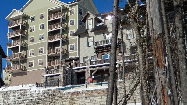 A multi-story hotel with balconies, a stone retaining wall, and a snowy landscape. - 2 Br: Soaring Eagle 211 (Snowshoe)