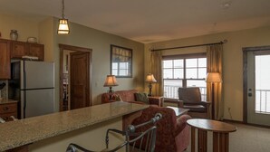 A compact kitchen with a refrigerator, a dining area with a table and chairs, a sofa, and a window with curtains. - 2 Br: Soaring Eagle 211 (Snowshoe)