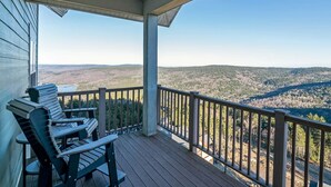 Une terrasse en bois avec deux fauteuils Adirondack donnant sur une vallée boisée.