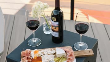 Une table avec une bouteille de vin, deux verres de vin rouge, un verre d’eau et une planche de fromages accompagnée de divers fromages et de charcuteries.