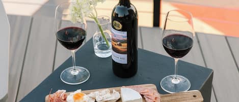 Una mesa con una botella de vino, dos copas de vino tinto, una copa de agua y una tabla de quesos y embutidos.