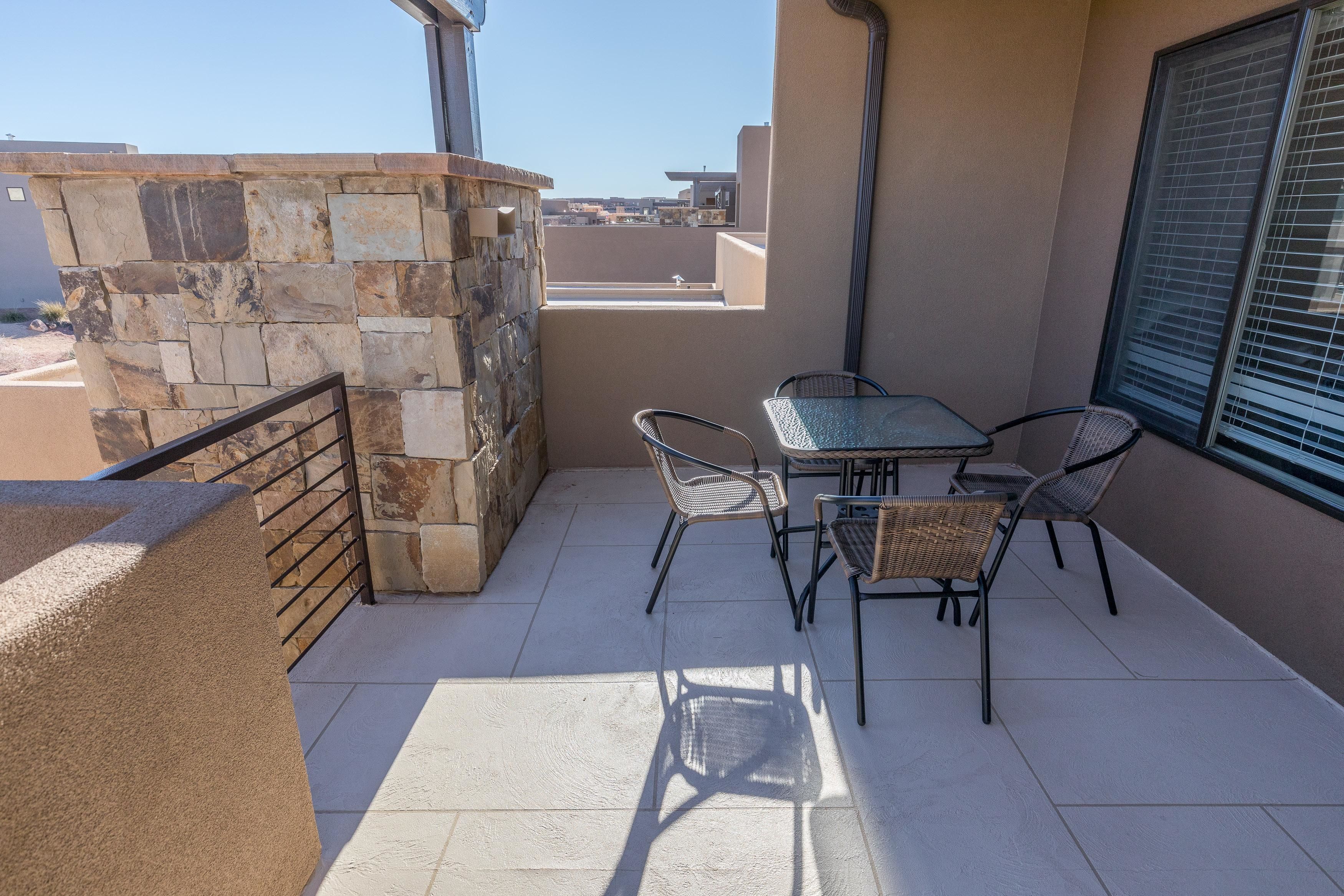 A balcony with stone walls, a table with chairs, and a window with blinds.