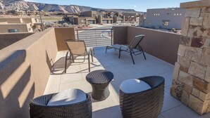 A rooftop terrace with wicker furniture, a stone wall, and a view of a residential area with mountains in the background. - Sunny Ledgeview Retreat (St. George)