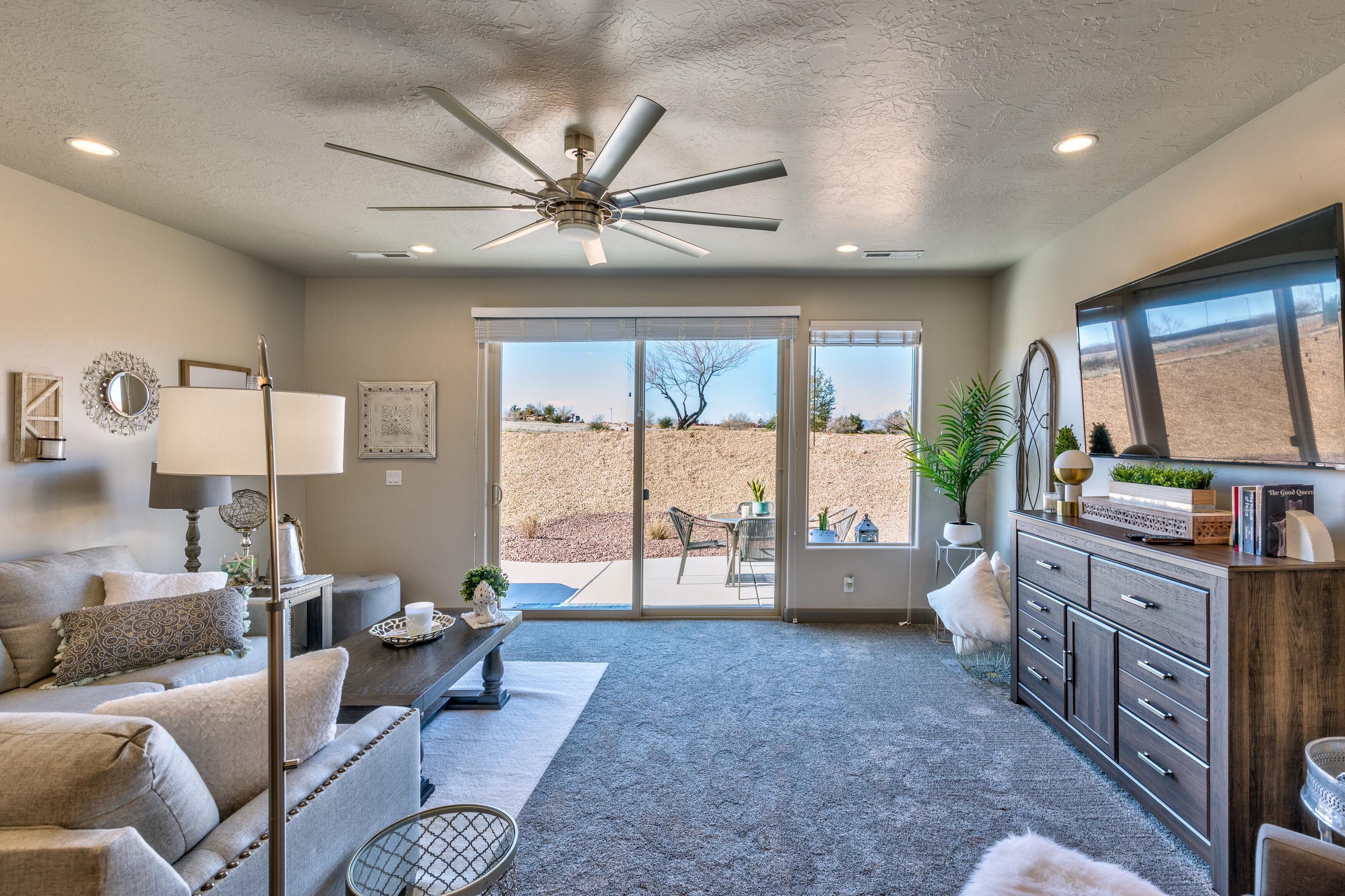 A living room with a ceiling fan, a sofa, a coffee table, a fireplace, and a view through the glass doors.