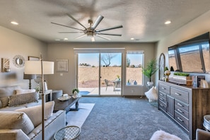 A living room with a ceiling fan, a sofa, a coffee table, a fireplace, and a view through the glass doors. - Fun At The Ledges (St. George)