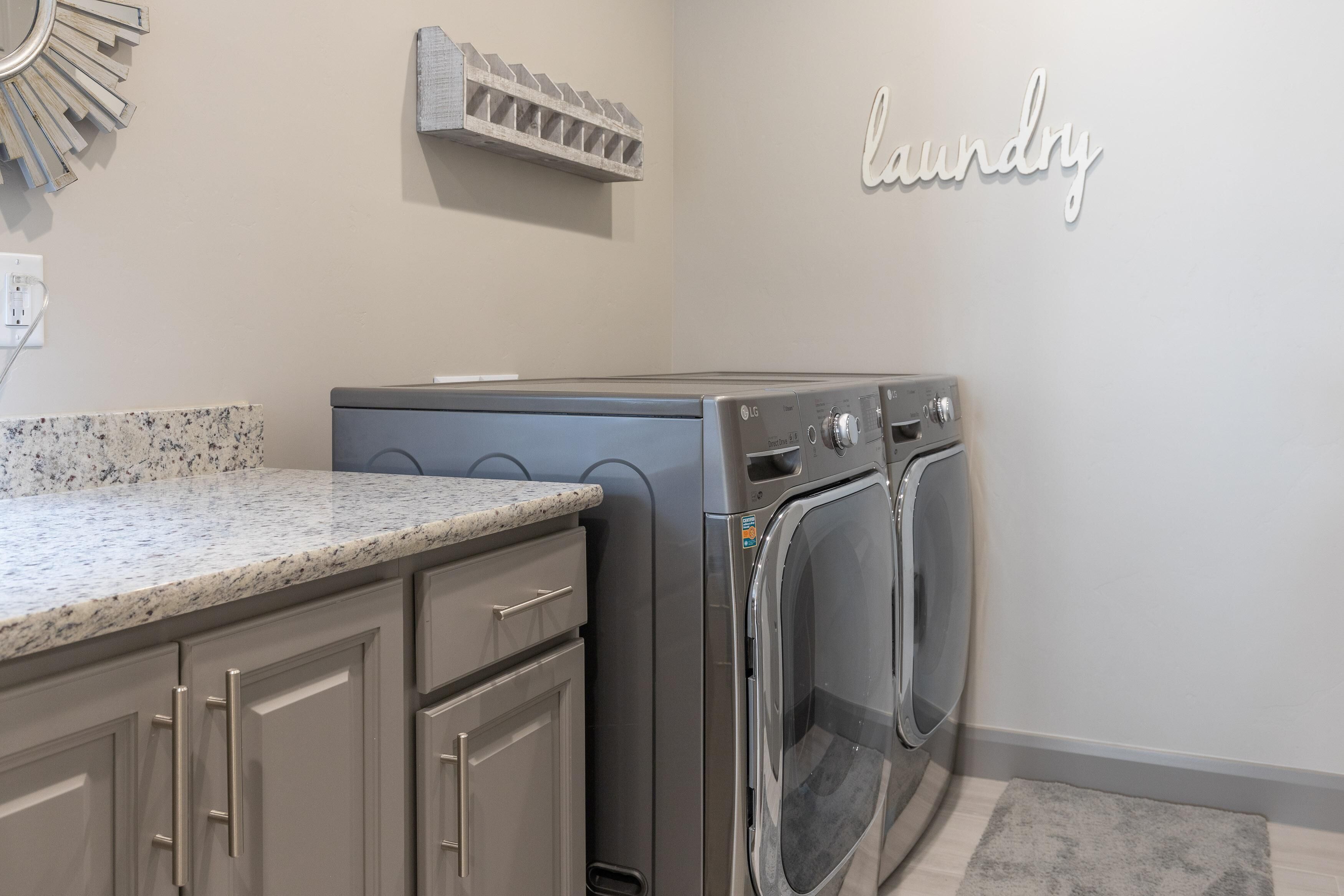 A laundry area with a washing machine and dryer, a granite countertop, and a wall-mounted laundry sign.
