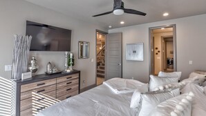 A bedroom with a bed, dresser, mirror, ceiling fan, and a hallway leading to a staircase. - Fun At The Ledges (St. George)