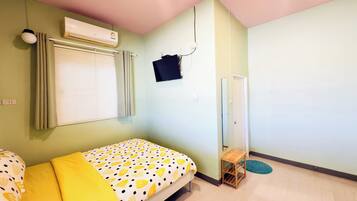 Una habitación con cama, aire acondicionado, ventana con persianas, una mesita y una puerta.