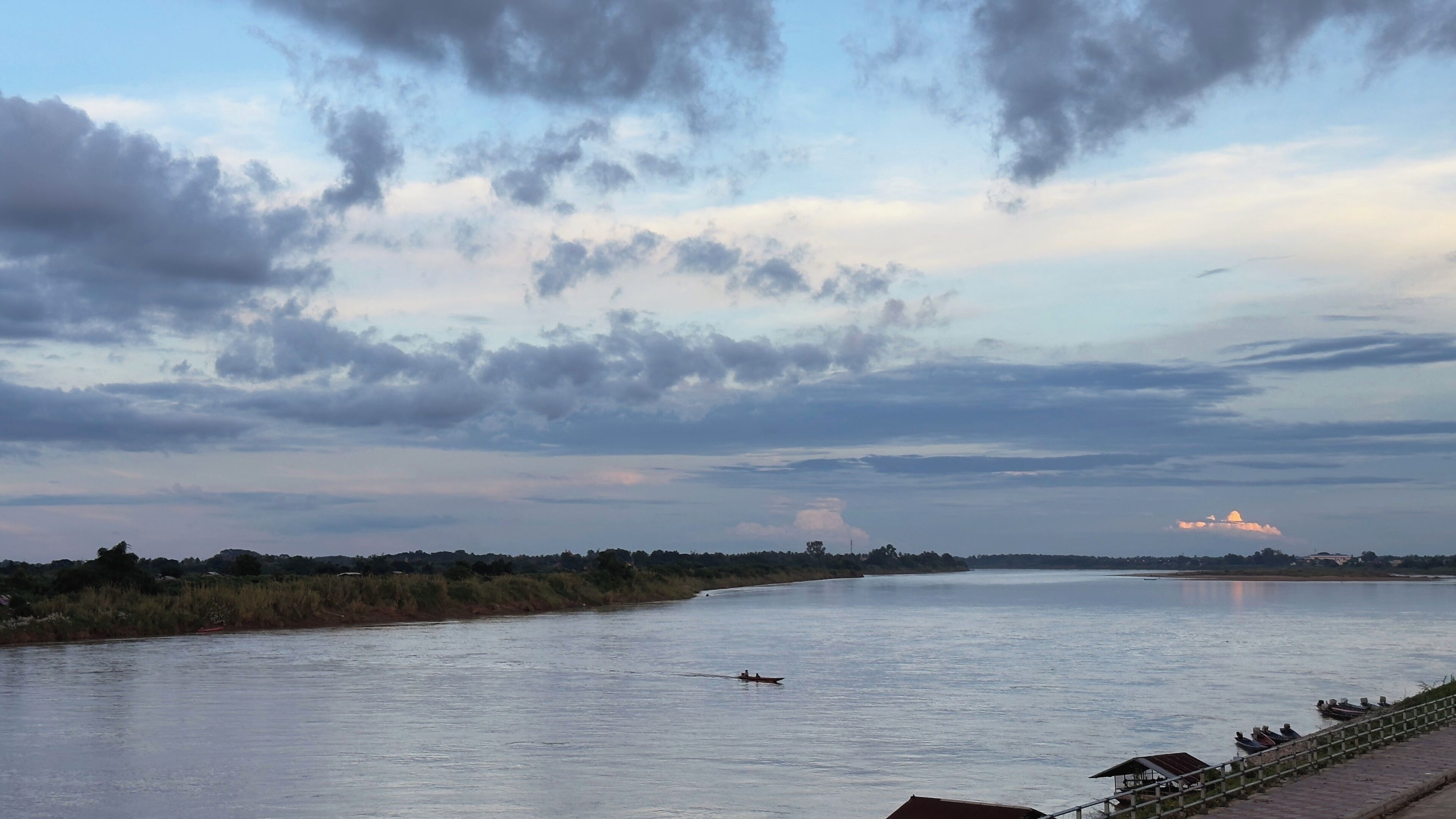 A river with a boat in the middle, surrounded by trees and a cloudy sky.