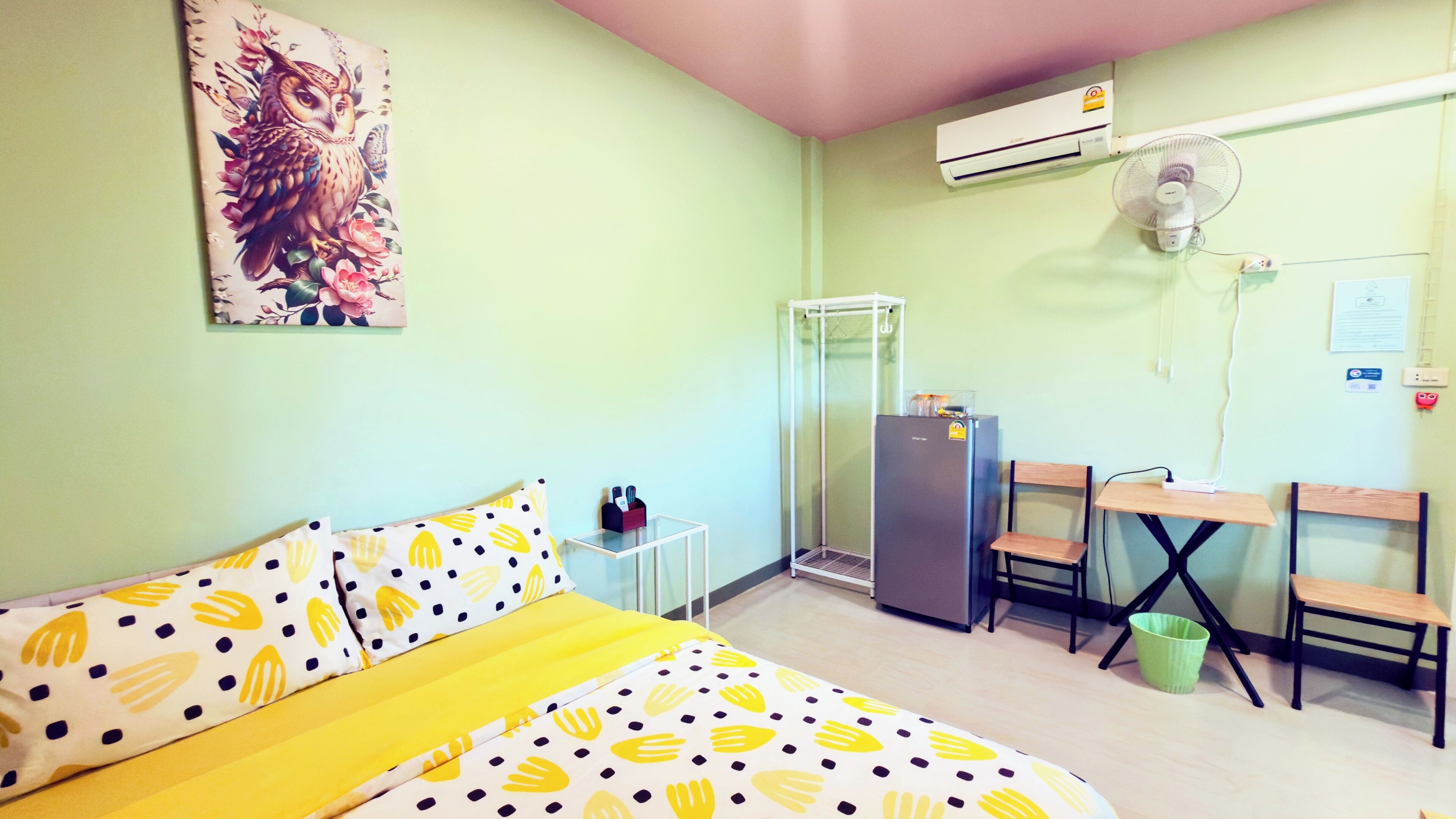 A small room with a bed, a desk, a chair, a refrigerator, and an air conditioning unit.