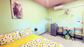 A small room with a bed, a desk, a chair, a refrigerator, and an air conditioning unit.