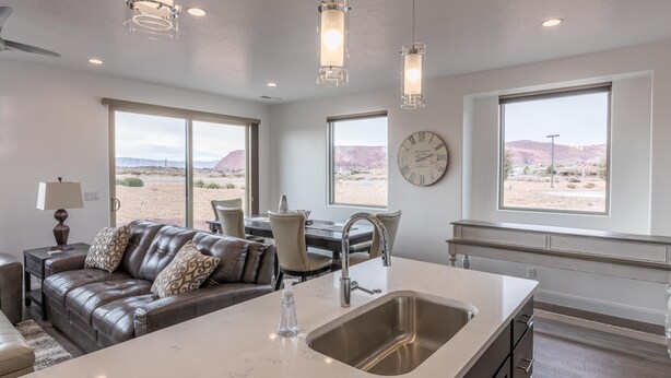 A modern kitchen with a large island, a dining area with a table and chairs, and large windows offering a desert view. - Canyon Views (St. George)