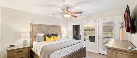 A bedroom with a bed, nightstand, ceiling fan, and a view through a door.