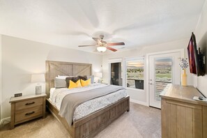 A bedroom with a bed, nightstand, ceiling fan, and a view through a door. - A Gathering Place (St. George)