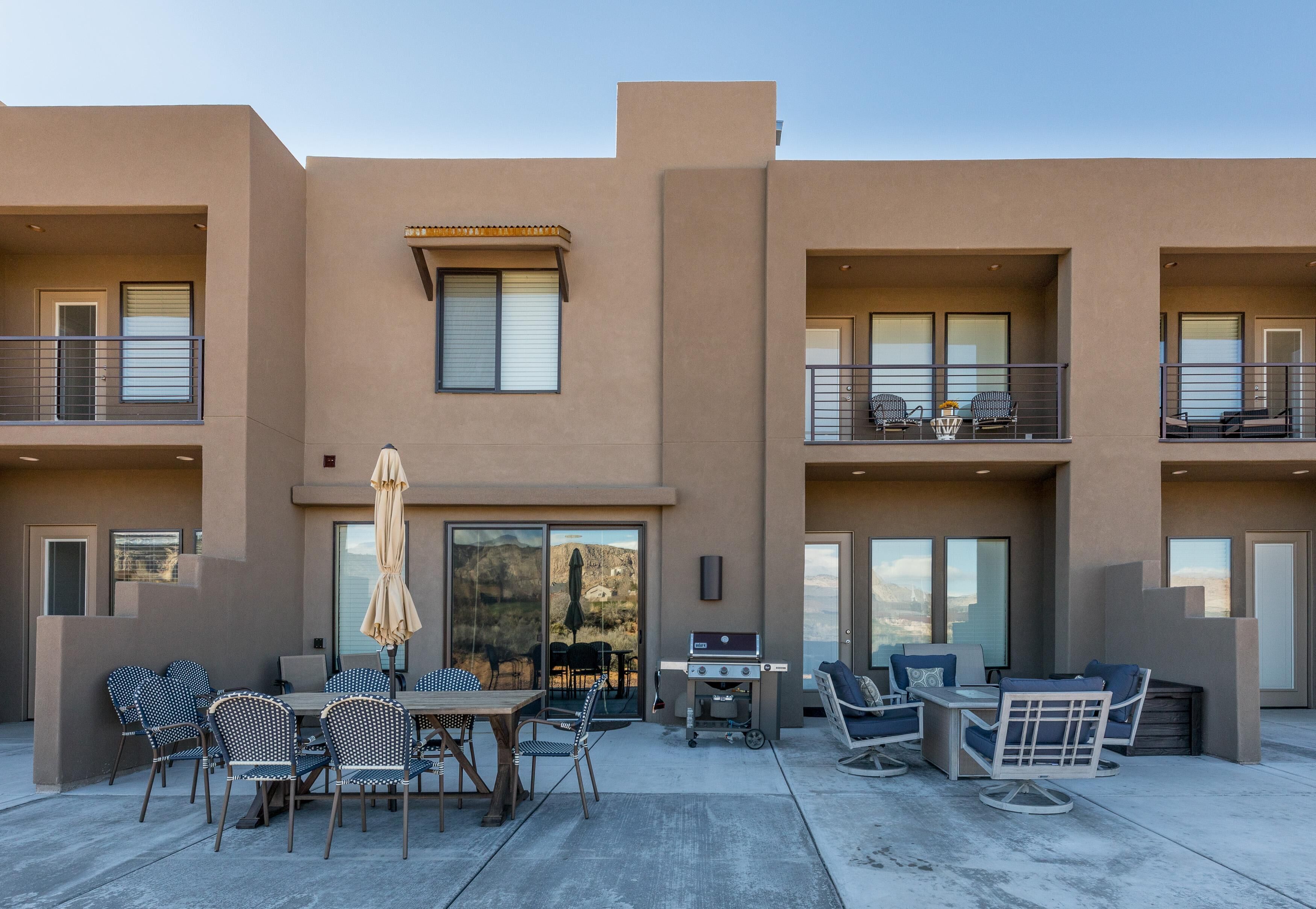 A modern building with a patio area featuring outdoor furniture, a grill, and a view of the landscape.