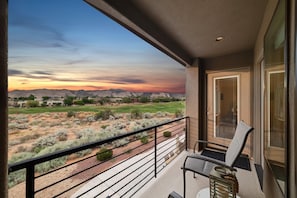 A balcony with a view of a desert landscape at sunset, a door, and a chair. - A Gathering Place (St. George)