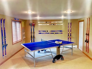 A room with two ping pong tables, skis, and a sign indicating 'WOMEN'S HOME'. - W62 Mount Wash Place Townhome, AC, seasonal views, fireplace, large deck, yard, and ping pong! (Bretton Woods)