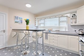 A modern kitchen with a bar area, white cabinets, and a tiled floor. - 10 Ballybane (Galway)