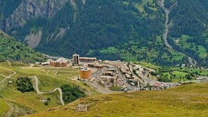 A mountainous town with a central building complex surrounded by green fields and a winding road.