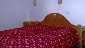 A bedroom with a wooden bed frame, a red bedspread with white patterns, two bedside tables, and wall-mounted lamps.