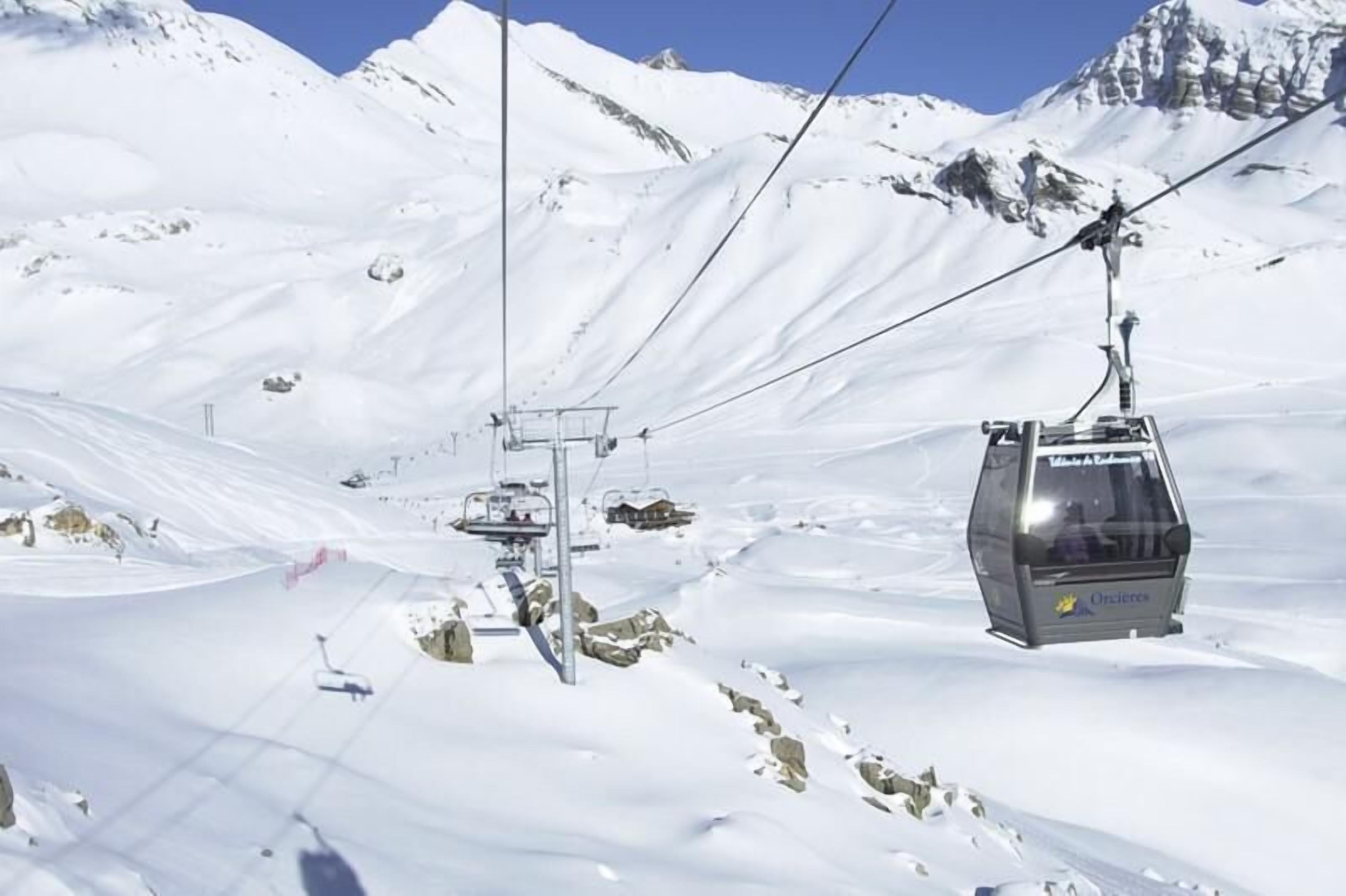 A ski lift chair moving along a snowy mountain path with cables overhead.