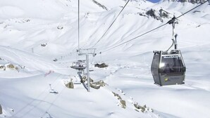 A ski lift chair moving along a snowy mountain path with cables overhead.