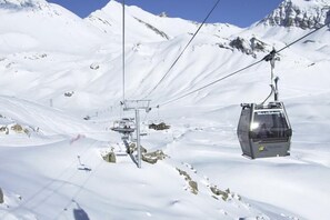 A ski lift chair moving along a snowy mountain path with cables overhead.