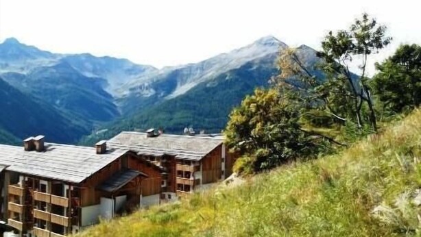 A mountain lodge with multiple wooden cabins, a ski lift, and a backdrop of snow-capped mountains.