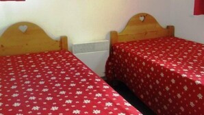 A room with two wooden beds, each with a red floral bedspread and a heart-shaped decoration on the headboard.