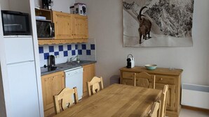 A compact kitchen with wooden cabinets, a microwave, a toaster, and a kettle. A dining table with chairs is in the center.