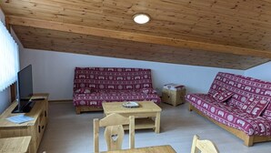A cozy room with a wooden ceiling, two patterned sofas, a small wooden table, and a TV on a wooden stand.