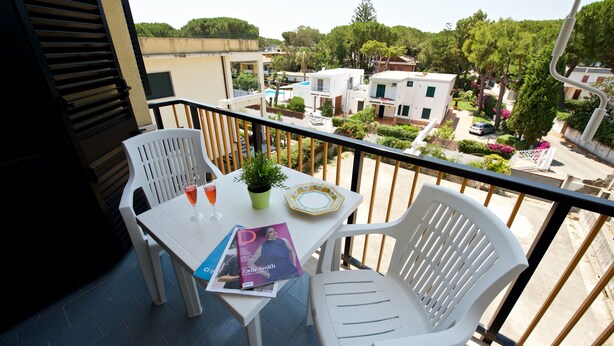 Ein Balkon mit zwei weißen Stühlen, einem Tisch und einer Zeitschrift.